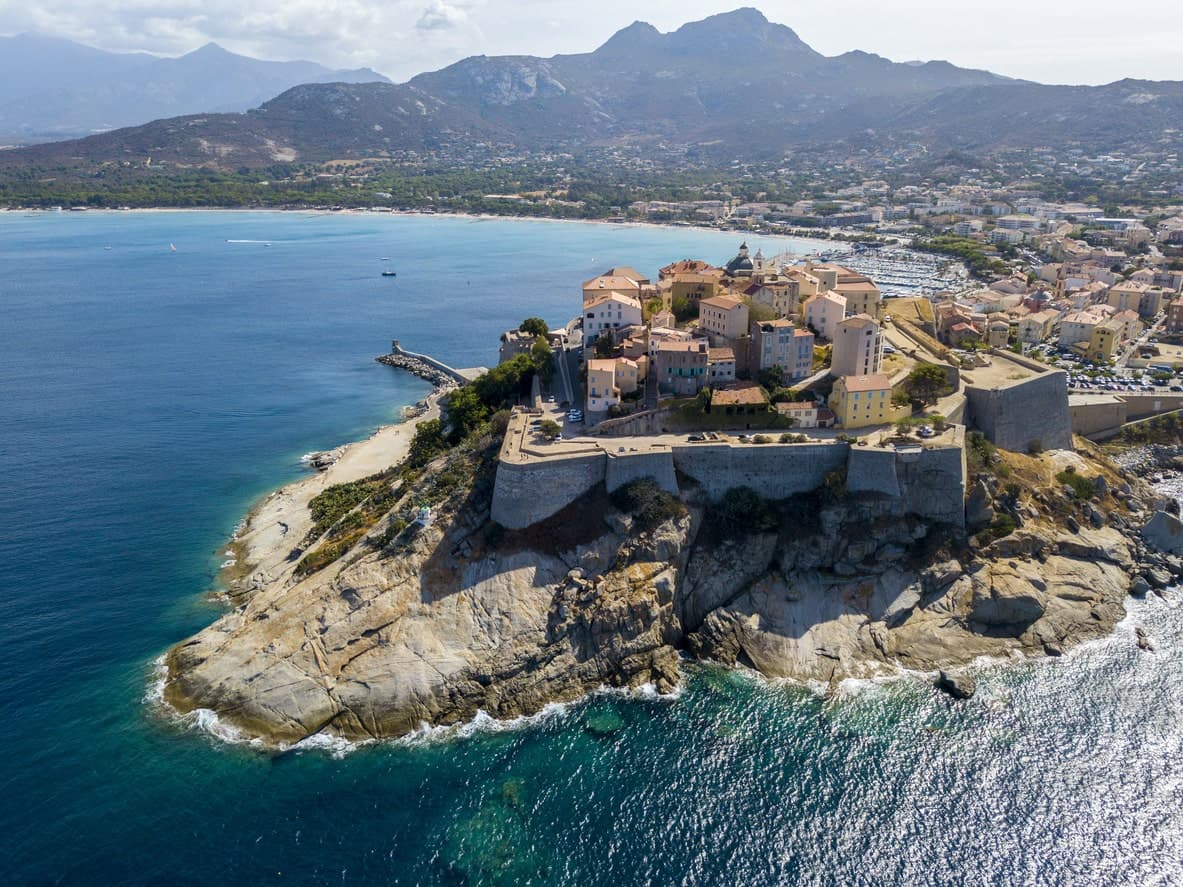 Luftaufnahme der Zitadelle von Calvi auf Korsika, umgeben von Meer und Bergen.
