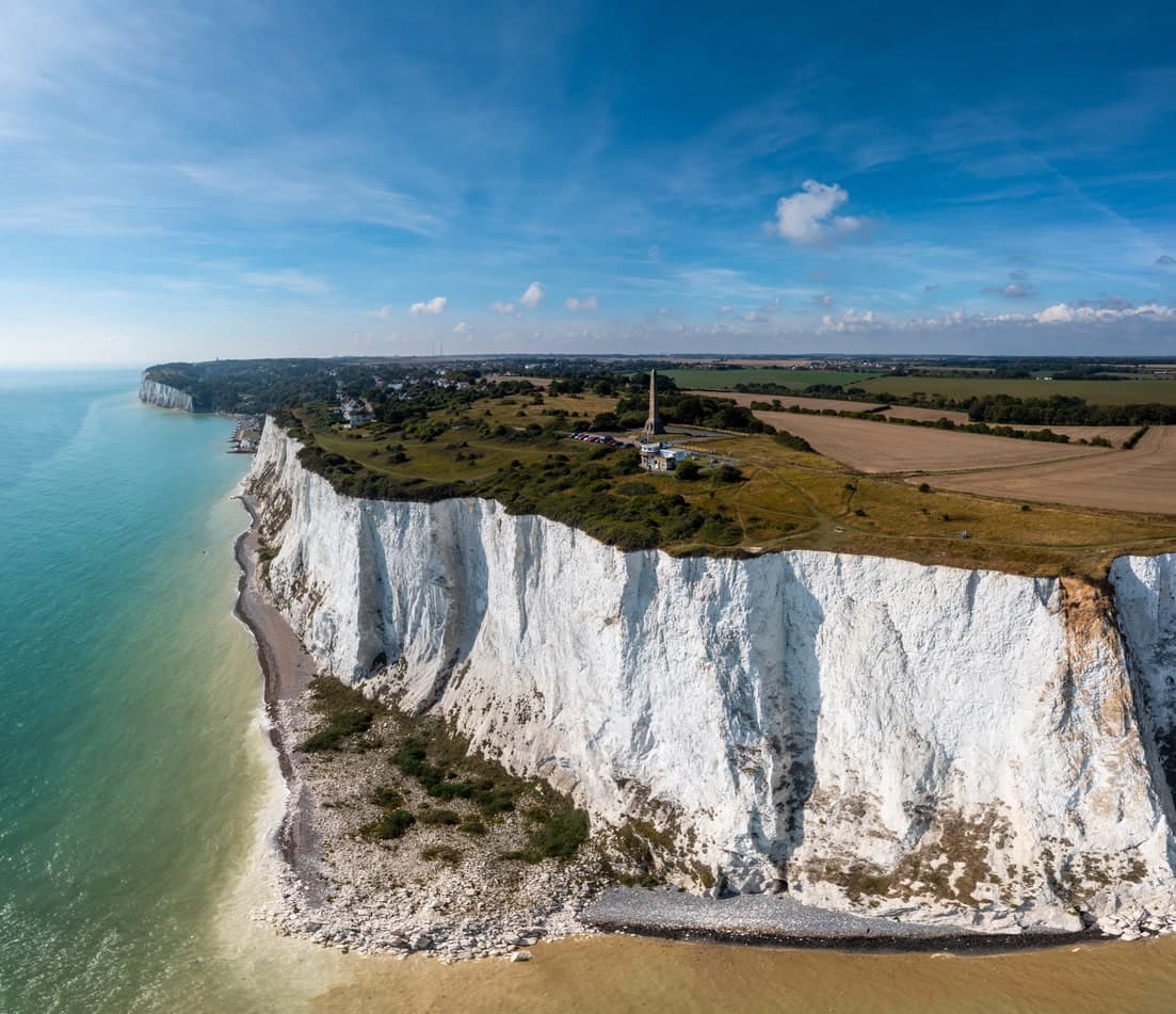 Luftaufnahme der weißen Klippen von Dover, umgeben von blauem Meer und grünen Feldern.