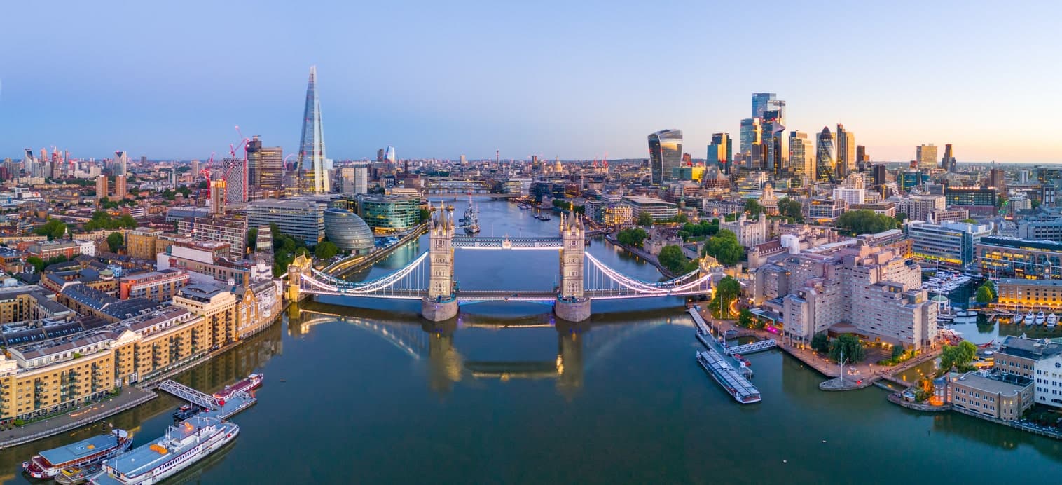 Luftaufnahme von London mit beleuchtetem Tower Bridge und Skyline bei Sonnenuntergang.