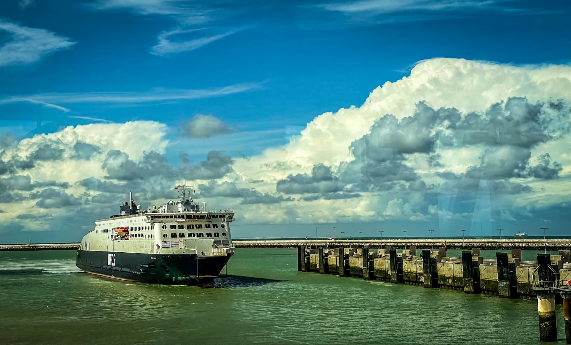Eine DFDS-Fähre läuft in den Hafen von Calais in Frankreich ein; dramatische Wolken und ruhiges Wasser.