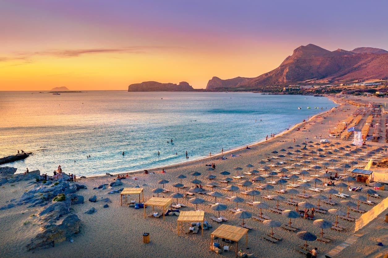 Strand auf Kreta bei Sonnenuntergang mit Liegen, Sonnenschirmen und sanftem Meer im Hintergrund.