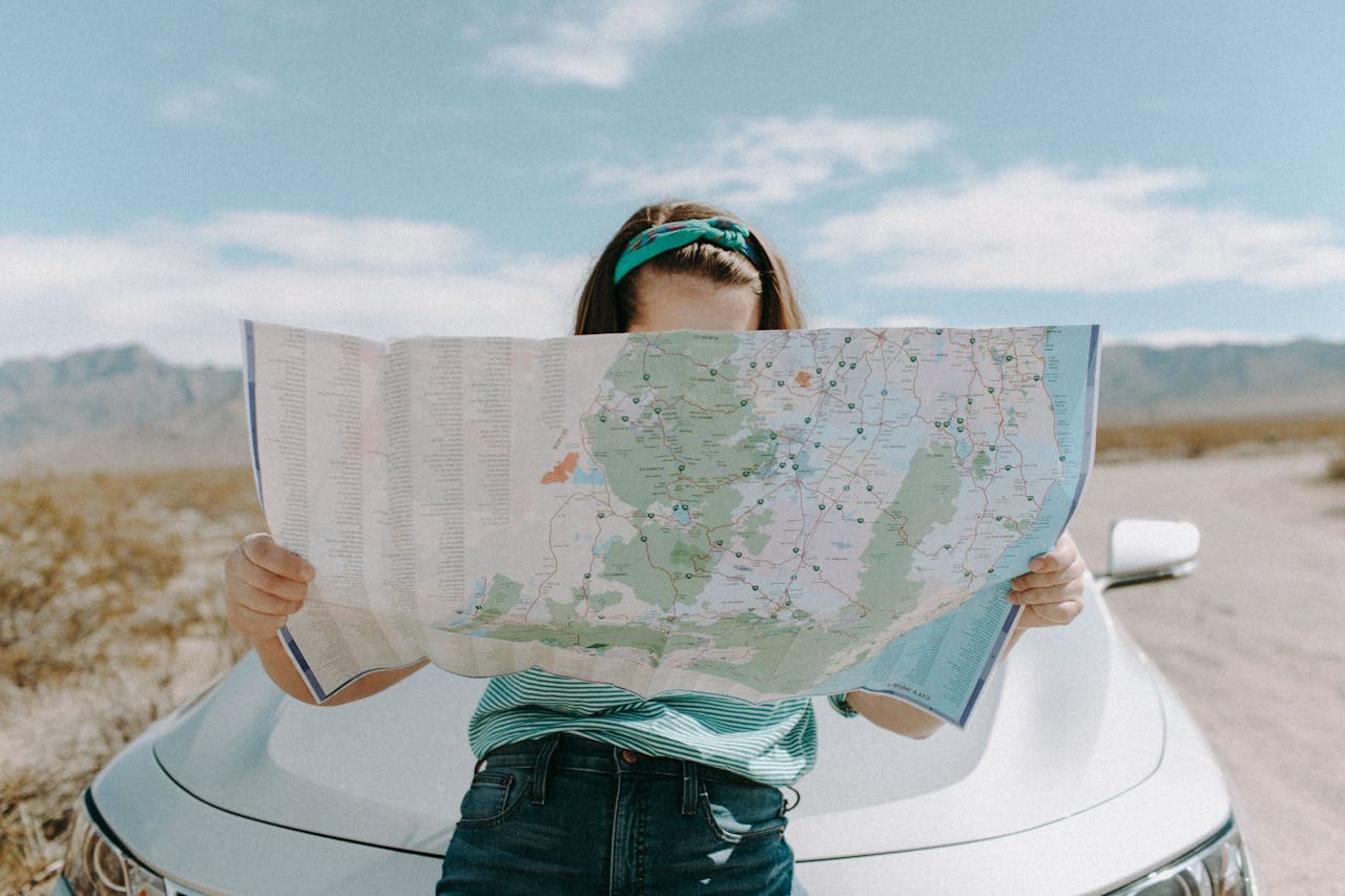 A young woman checking her routes on a map by her car.