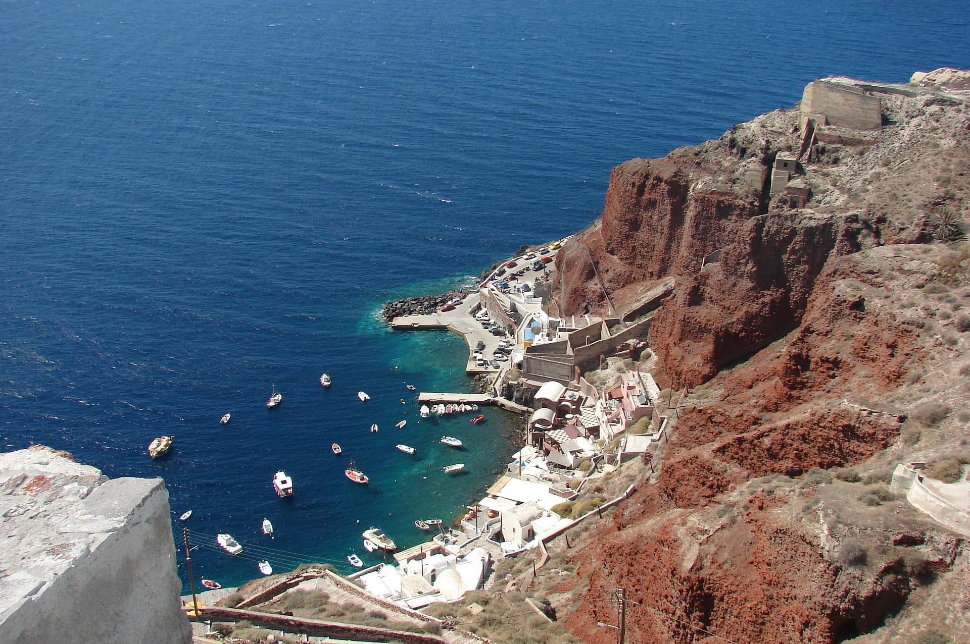 Veduta del porto di Ammoudi a Santorini con barche ormeggiate, scogliere rosse e mare blu