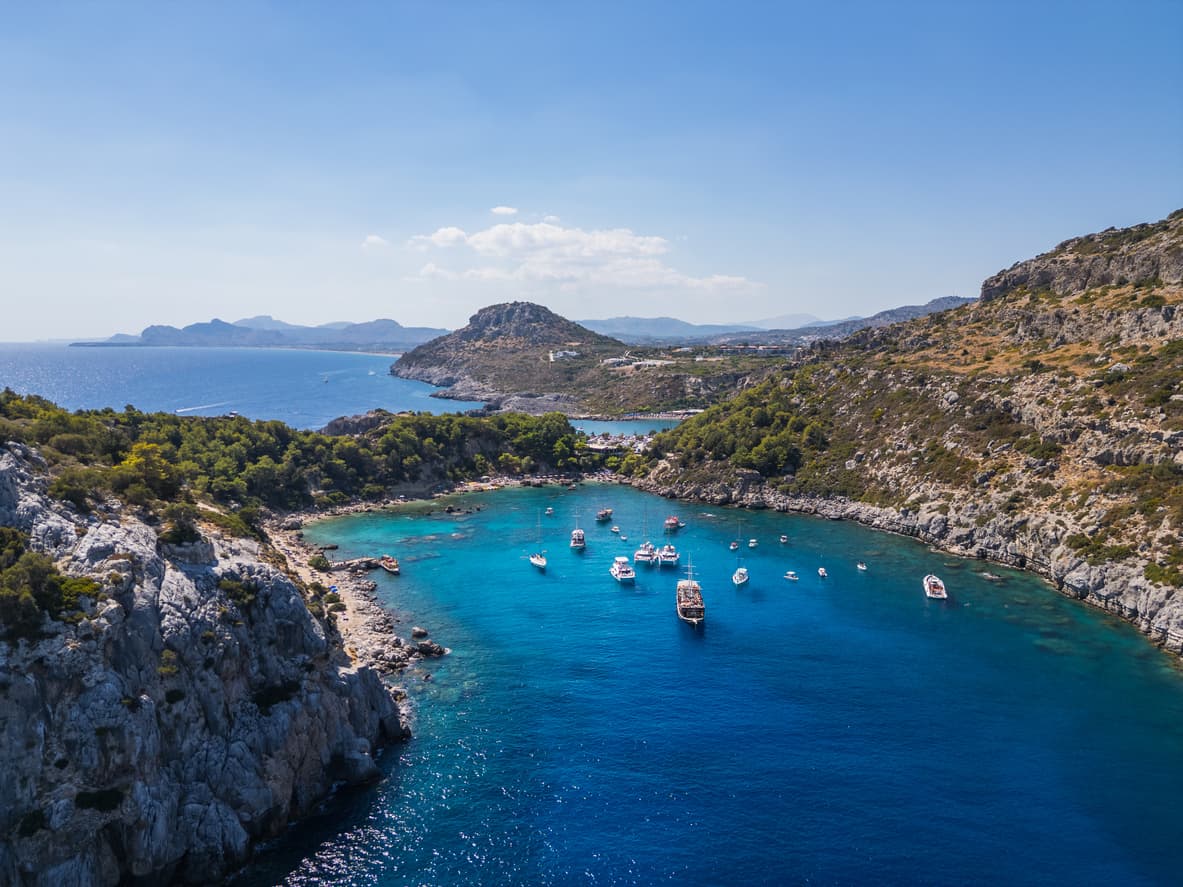 A daytime drone photo of Rhodes. In addition to the blue sea and sky, boats are visible on the water.