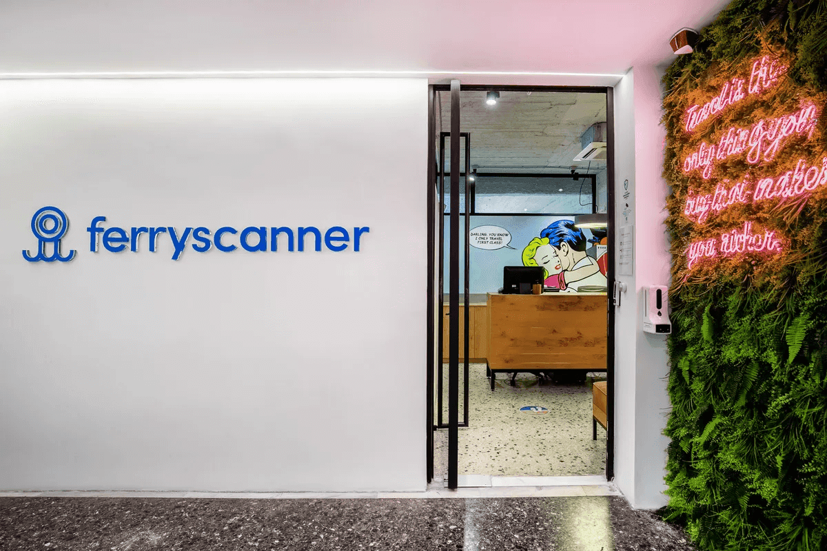 A Ferryscanner iroda bejárata egy fehér falat mutat a Ferryscanner logójával, egy üvegajtót, ami a hallba vezet, ahol pop art fali dekoráció vár, és jobbra egy zöld, függőleges kertfal kap helyet, amit egy rózsaszín neonfény világít meg ezzel az üzenettel: Travel is the only thing you buy that makes you richer.