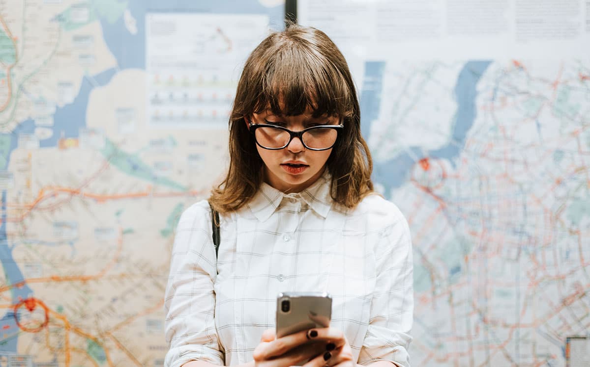 Traveler checking directions on a smartphone in front of a large transportation map.