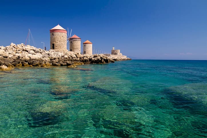 Arkaplanda üç yel değirmeni bulunan Rodos'un turkuaz suları