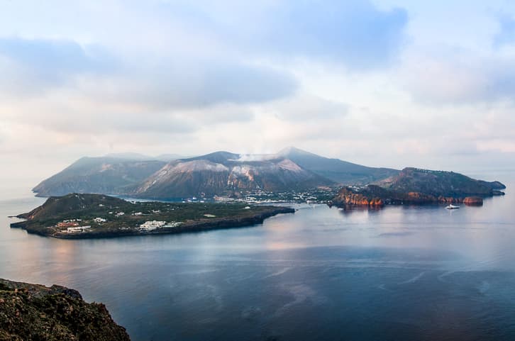 L'isola di Vulcano, una delle Isole Eolie, vista dall'alto in un momento di calma, con il mare placido che riflette il cielo nuvoloso
