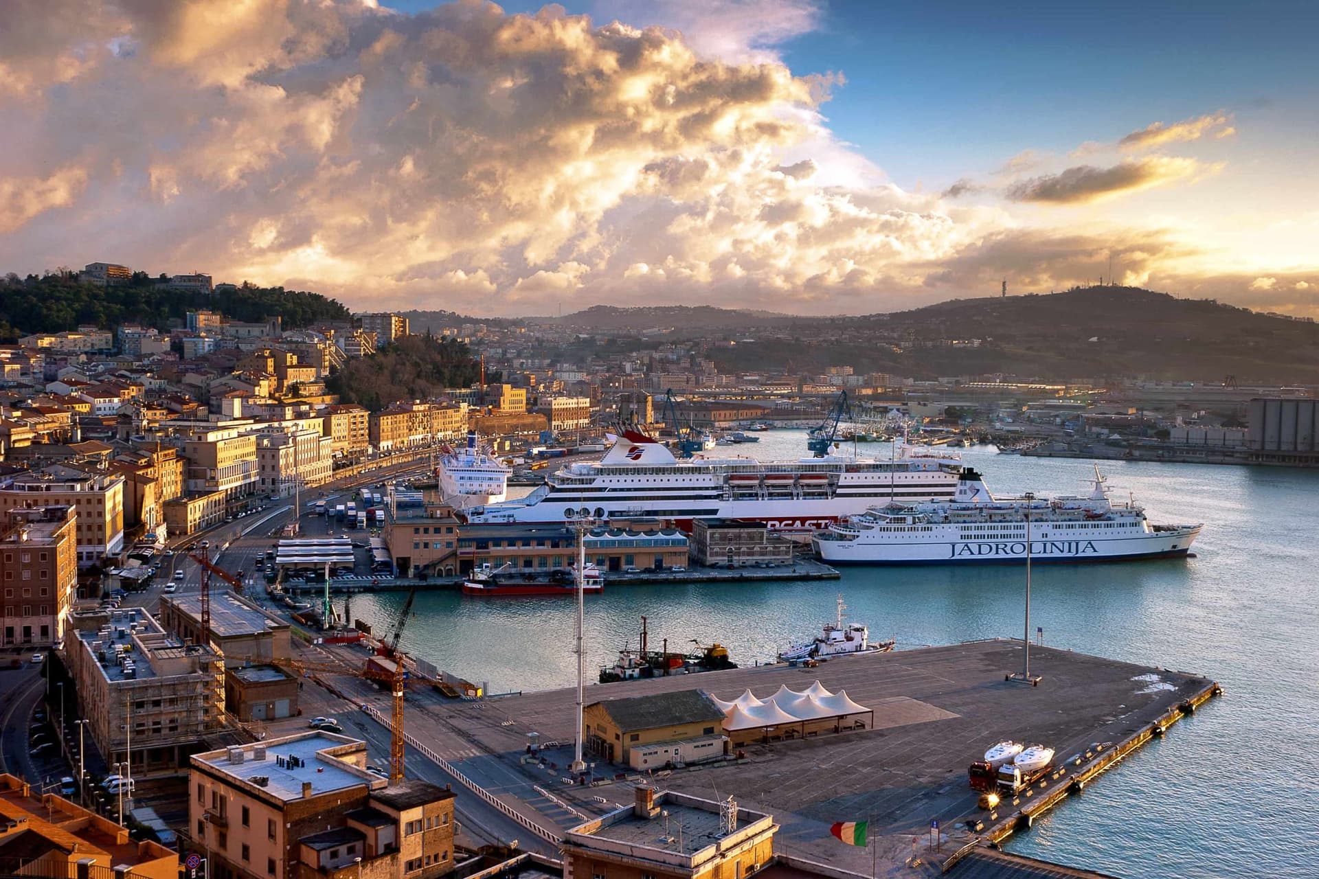 Veduta aerea di Ancona, Italia, con il suo vivace porto, i traghetti e una suggestiva collina panoramica sullo sfondo al tramonto.