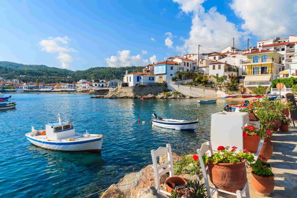 Blommor på stranden med fiskebåtar i hamnen i Kokkari på ön Samos, Grekland