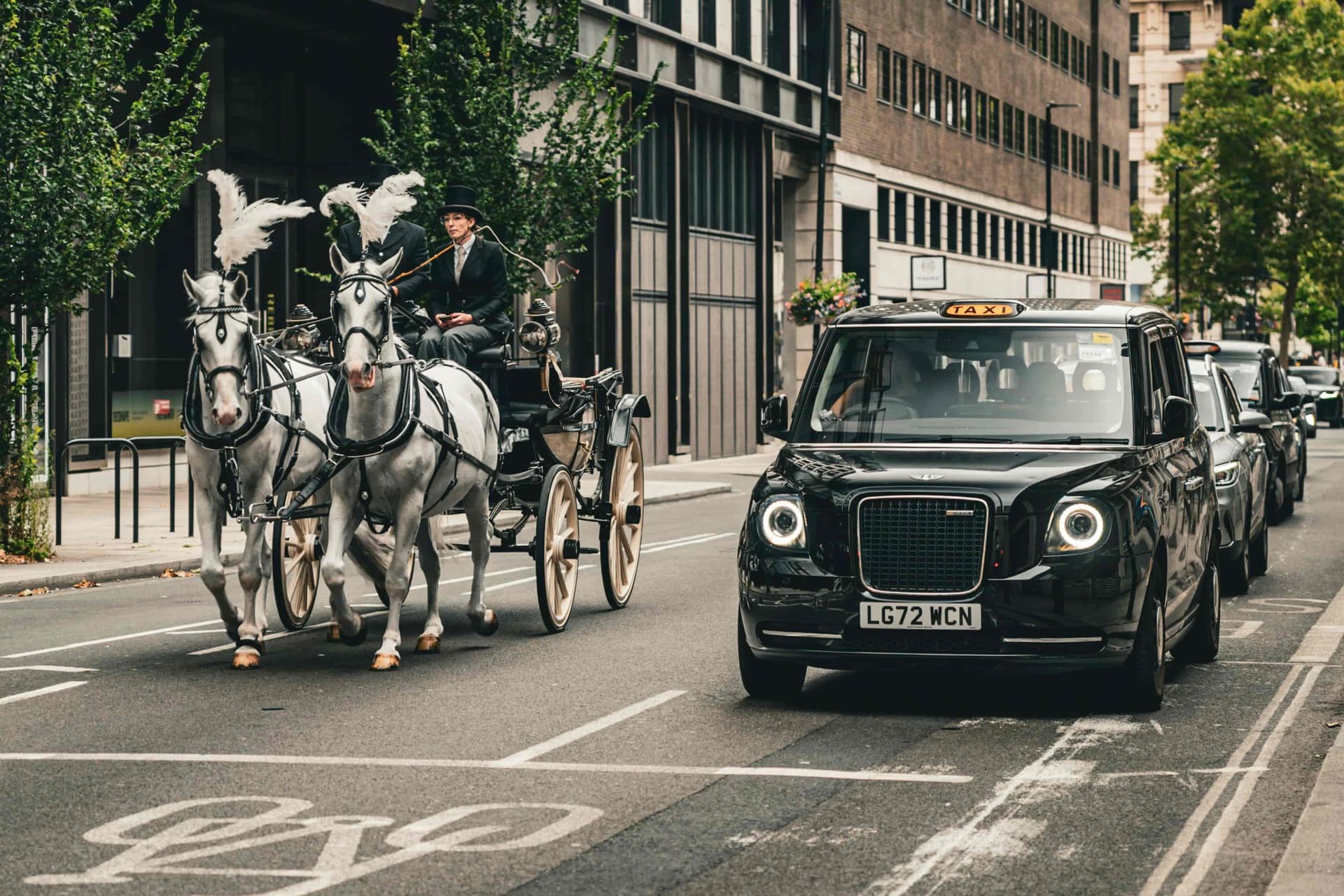 Ein typisches Londoner Taxi überholt eine von Pferden gezogene Kutsche in den Straßen Londons.